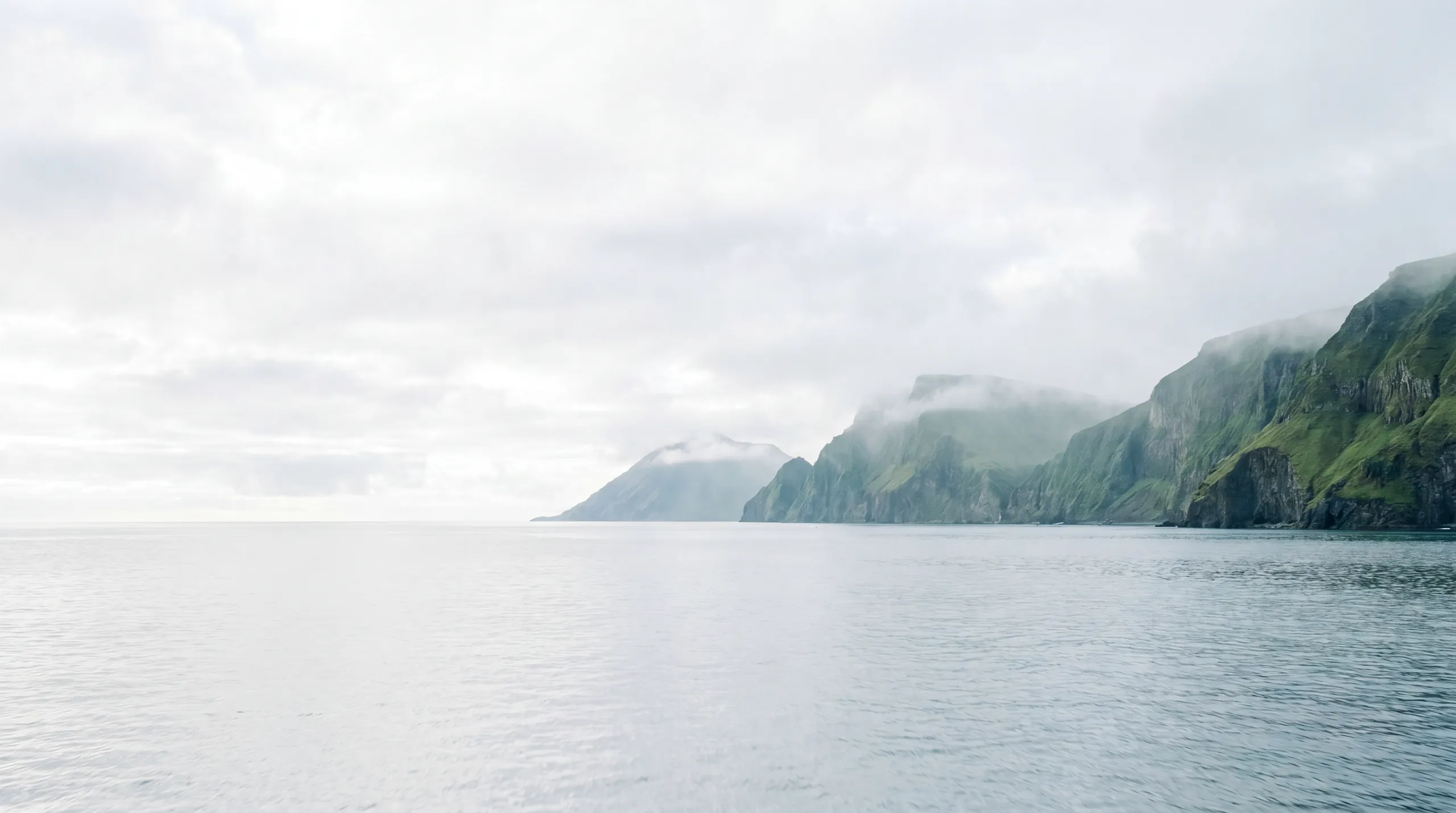 Mist over the calm East Sea with a cloud-wrapped, forested Korean coastline in the distance
